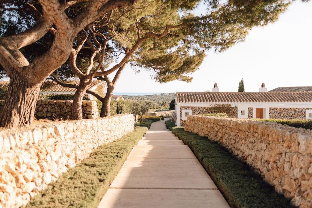 a sidewalk next to a stone wall with trees at Torralbenc, a Small Luxury Hotel of the World in Cala'n Porter