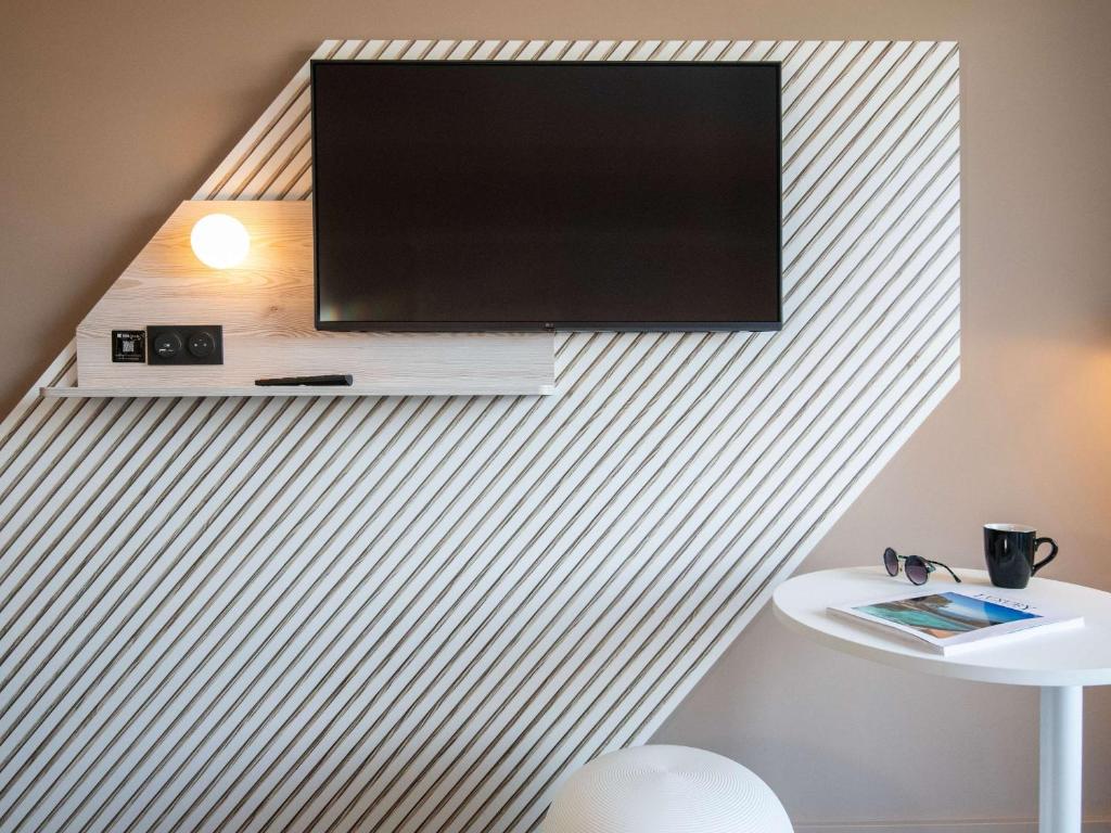 a flat screen tv hanging on a wall with a table at ibis Styles Porto Vecchio in Porto-Vecchio