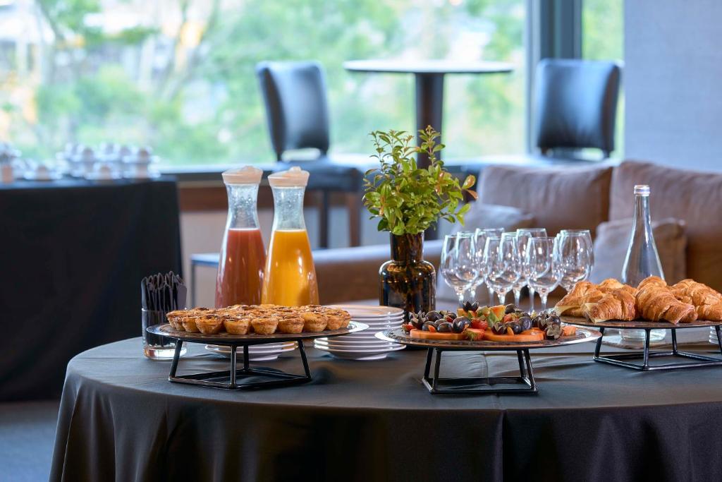 A close-up of a breakfast buffet with pastries, fruit, juices, and wine glasses by a window.