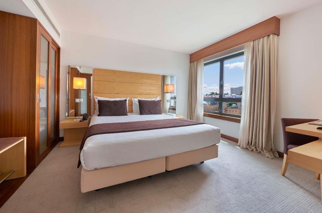 A bedroom with a large bed, generous window and separate desk area.