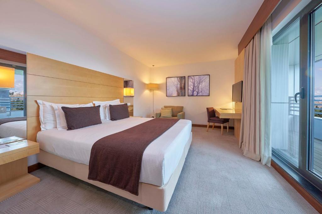 A large bedroom opening toward a sitting and work area beside full-height glazing.