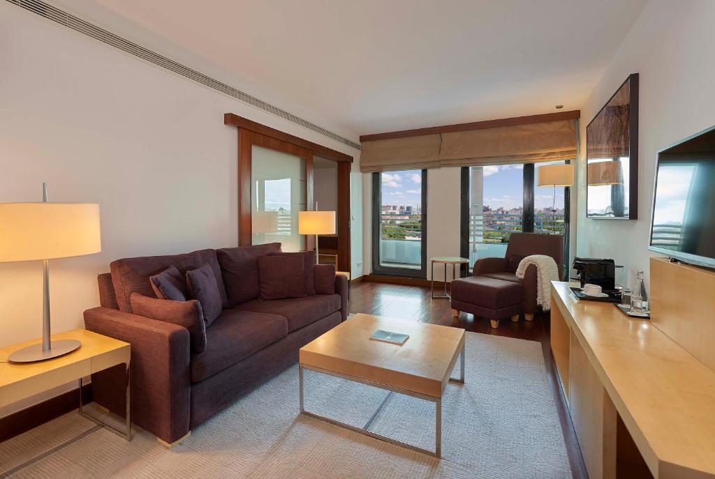 A living room with a sofa, television, coffee table and broad city-facing windows.