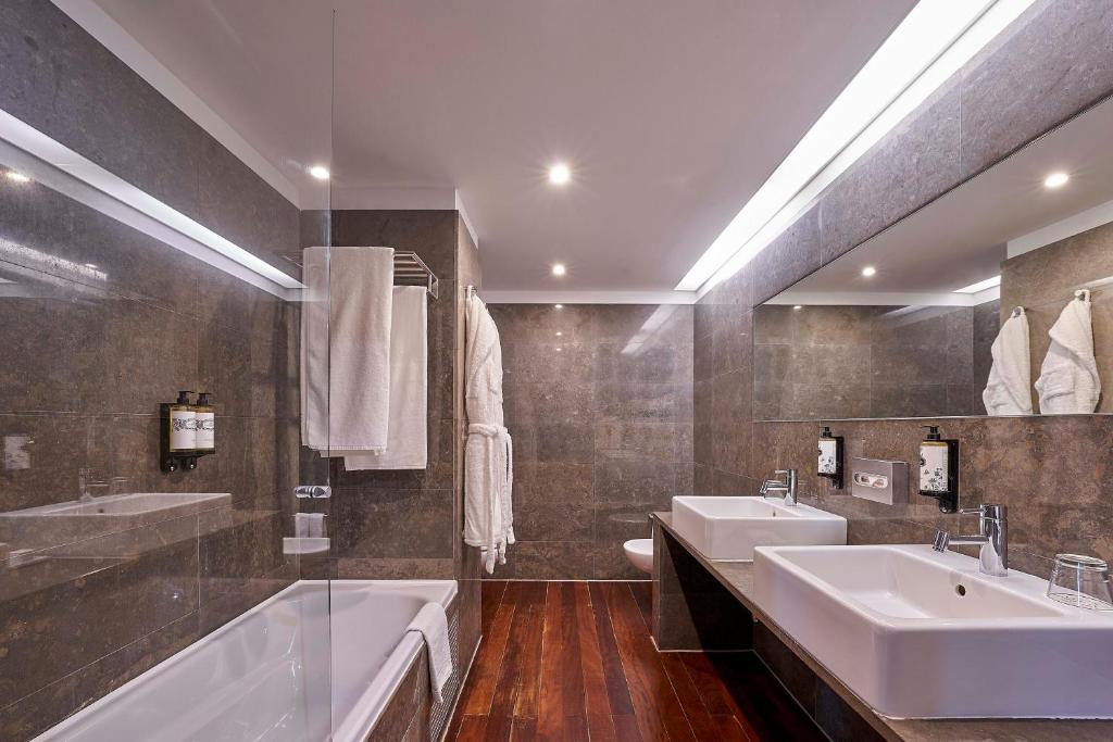 A polished marble bathroom with a bathtub, twin basins and a large mirror.