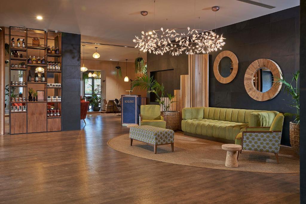 A spacious lounge lobby with a green sofa, patterned chairs, and a bar display.