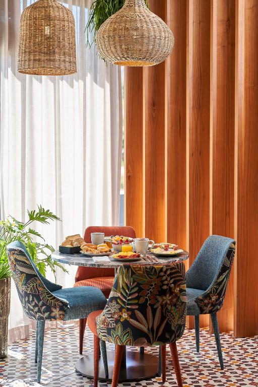 A small breakfast table is set beside tall windows with woven pendant lights and colorful upholstered chairs.