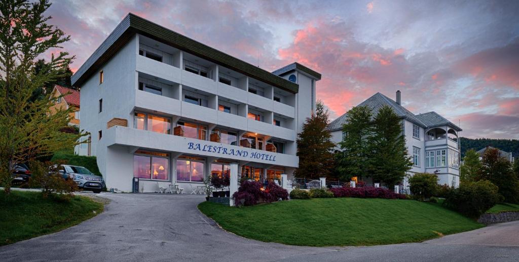 a large white building with a sunset in the background at Balestrand Hotel in Balestrand