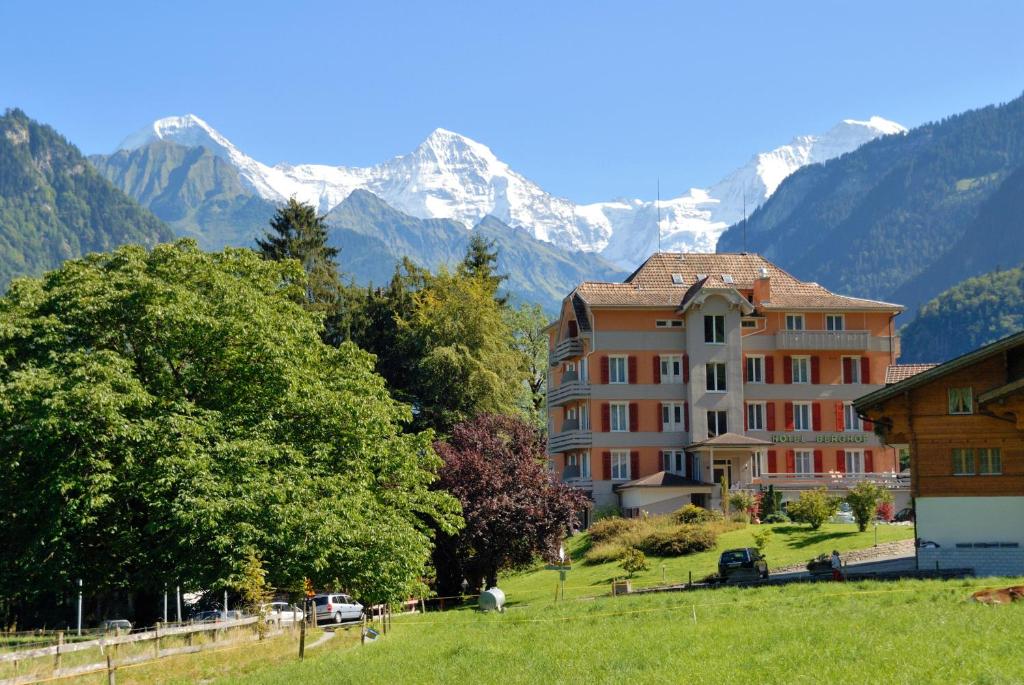 
a large building with trees and a mountain range at Hotel Berghof Amaranth in Wilderswil
