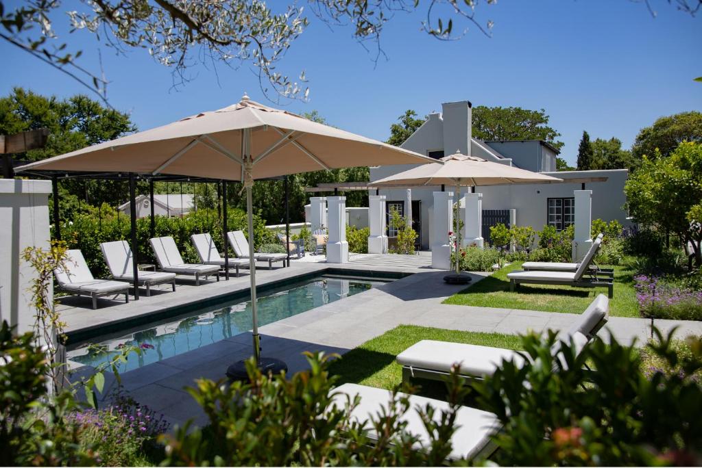 a pool with chairs and umbrellas next to a house at Macaron Boutique Guest House in Franschhoek