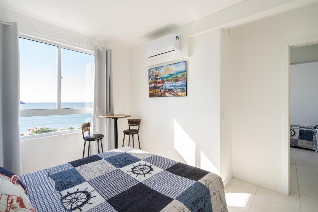 a white bedroom with a bed and a view of the ocean at Apartamentos em Bal Piçarras 150 M DA PRAIA com SACADA, WI-FI, PISCINA, PORTARIA 24h, PLAYGROUND e vaga de GARAGEM in Piçarras