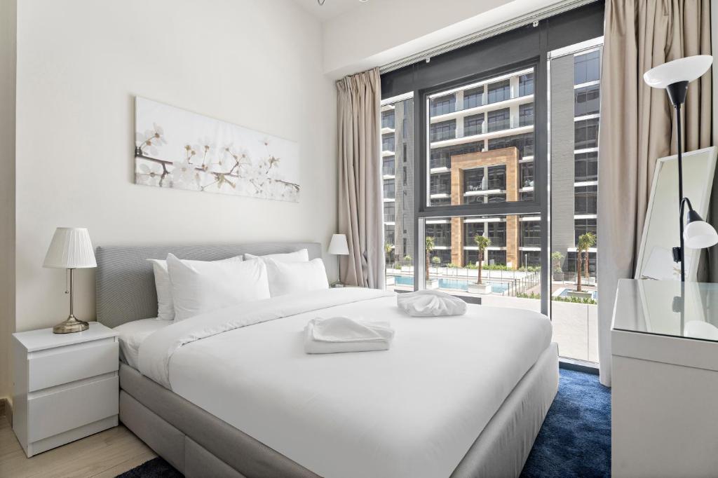 Un dormitorio blanco con una cama grande y una ventana. en Beautiful 1 BR with Gym, Pool & Kid's Playground, en Dubái