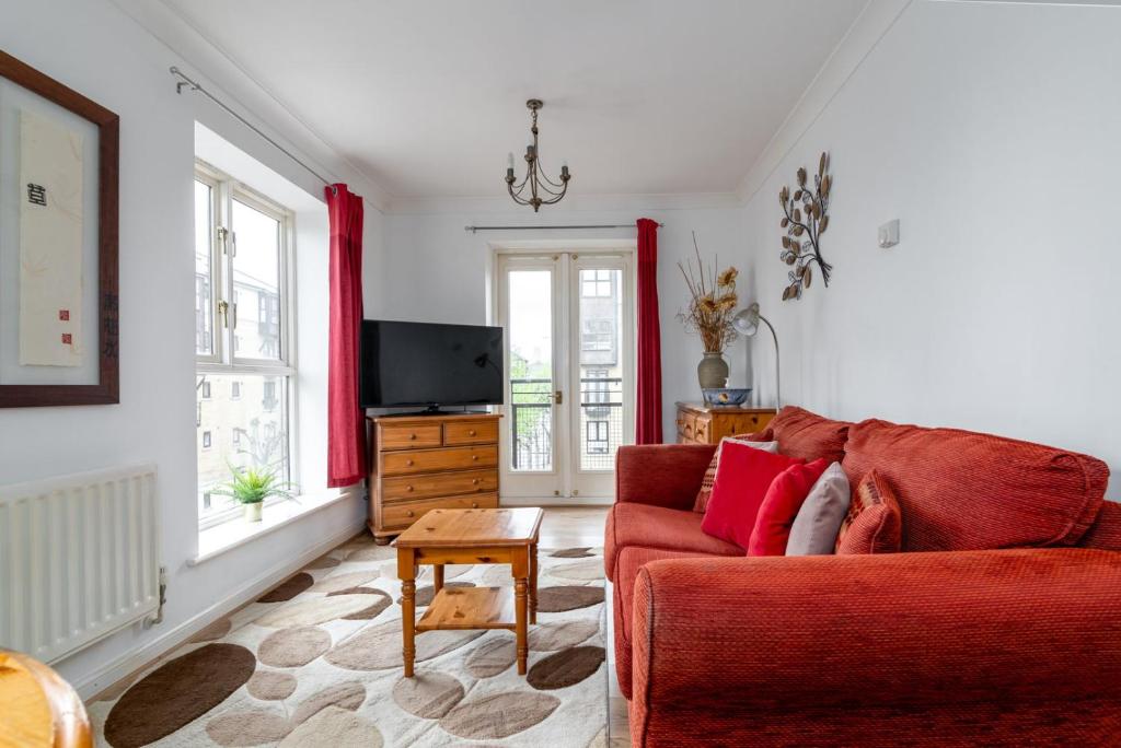 uma sala de estar com um sofá vermelho e uma televisão em GuestReady - Parkside getaway in Britannia Village em Londres