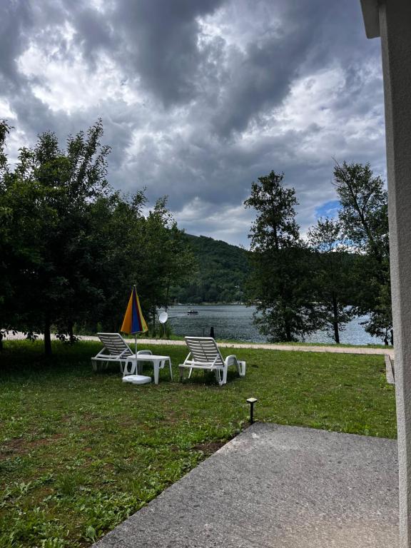 three chairs and an umbrella on the grass near a lake at Cobras Plivsko jezero, Jajce in Jajce