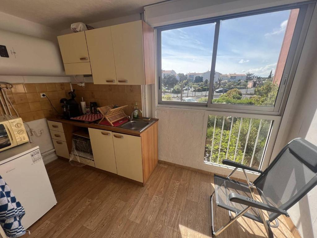 une cuisine avec une fenêtre et une chaise dans une pièce dans l'établissement JULES VERNE Agréable studio cabine Mt St Martin proche port Cap d'Agde, au Cap d'Agde