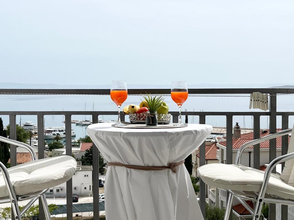 a table with two glasses of wine and fruit on a balcony at Apartments Irma in Baška Voda