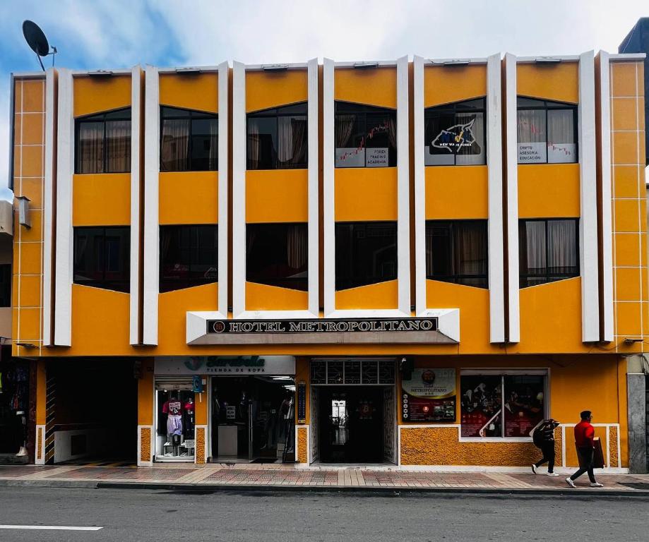 ein gelbes und weißes Gebäude mit Leuten, die auf der Straße spazieren in der Unterkunft Hotel Metropolitano in Loja
