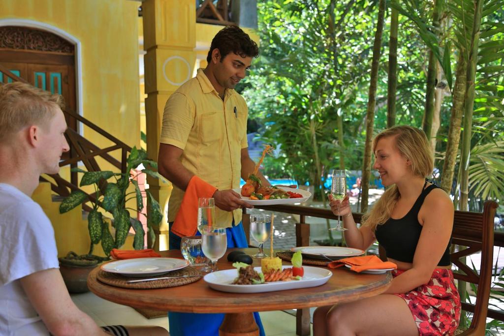 a man holding a tray of food at a table at Thambapanni Retreat in Unawatuna