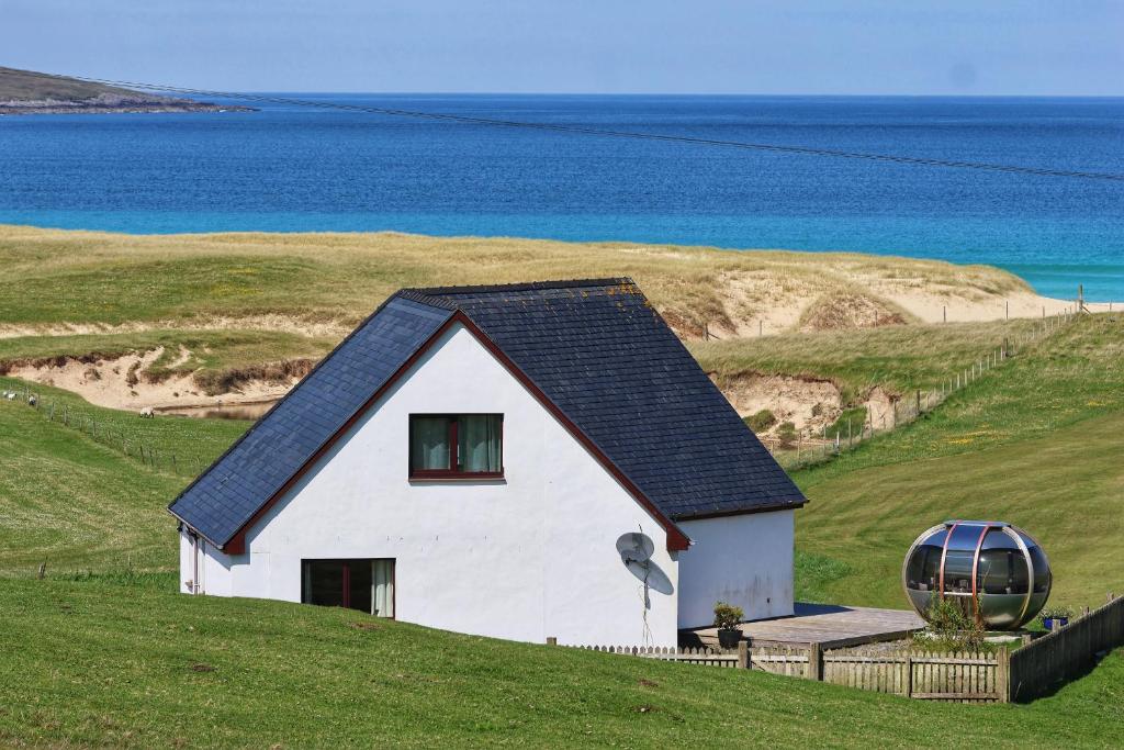 a small white house on a grassy hill next to the ocean at Corncrake Cottage in Manish