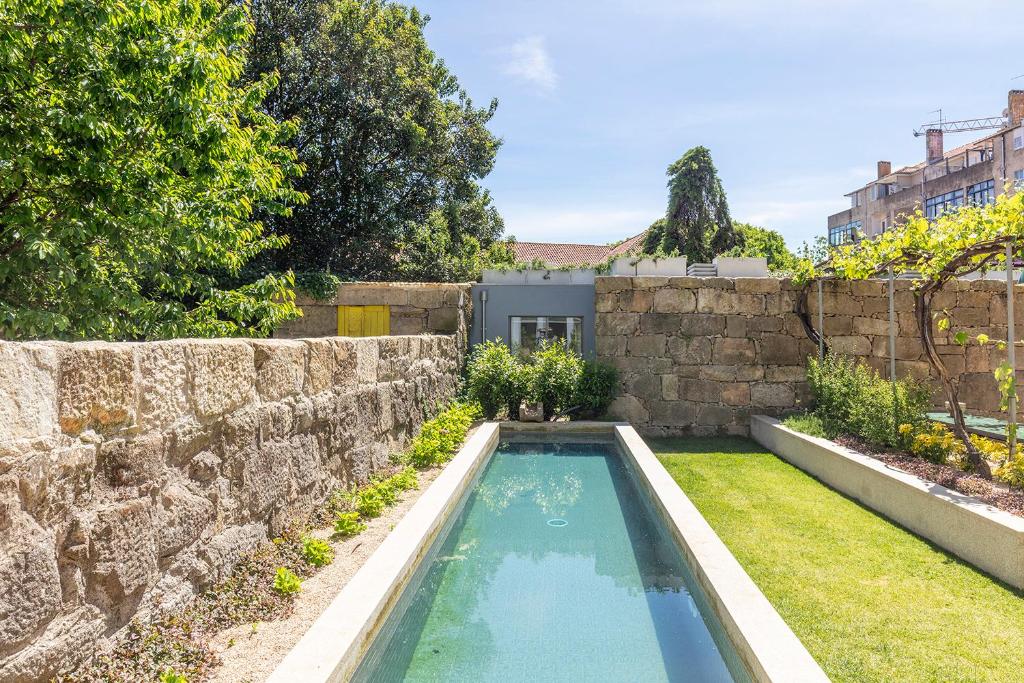 a swimming pool in a yard next to a stone wall at Vandoma in Porto