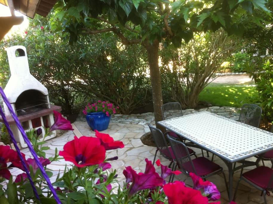 une terrasse avec une table et quelques fleurs rouges dans l'établissement APPARTEMENT de 50m2 en rez de jardin - 3 étoiles, à Porto-Vecchio