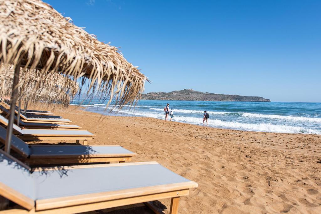 een rij strandstoelen met rieten parasols op een strand bij The Mini Beach Hotel in Stalós