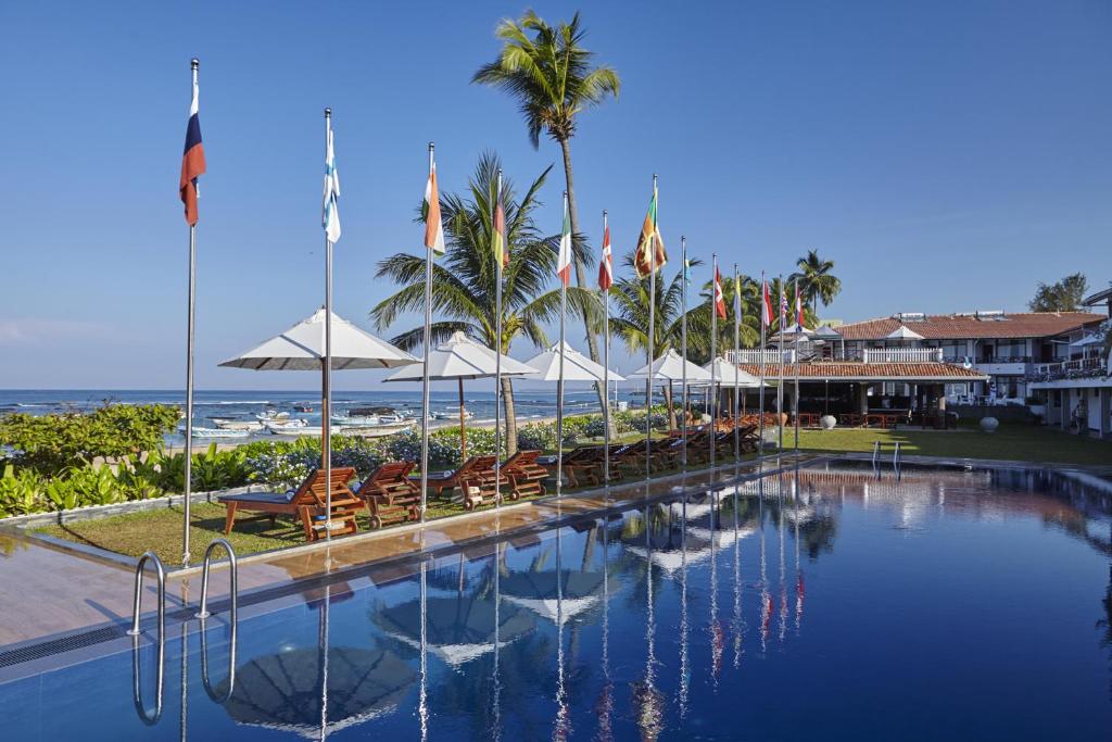 una piscina con sillas y sombrillas y la playa en Coral Sands Hotel, en Hikkaduwa