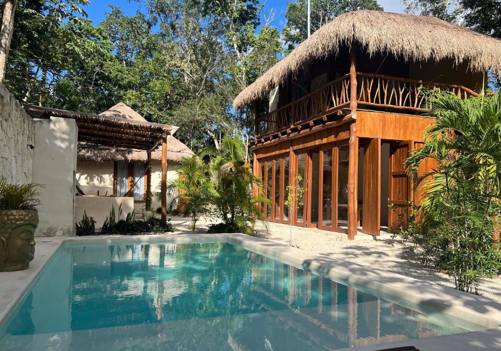 a house with a swimming pool and a thatch roof at Lodge Tzunum Jade in Tulum