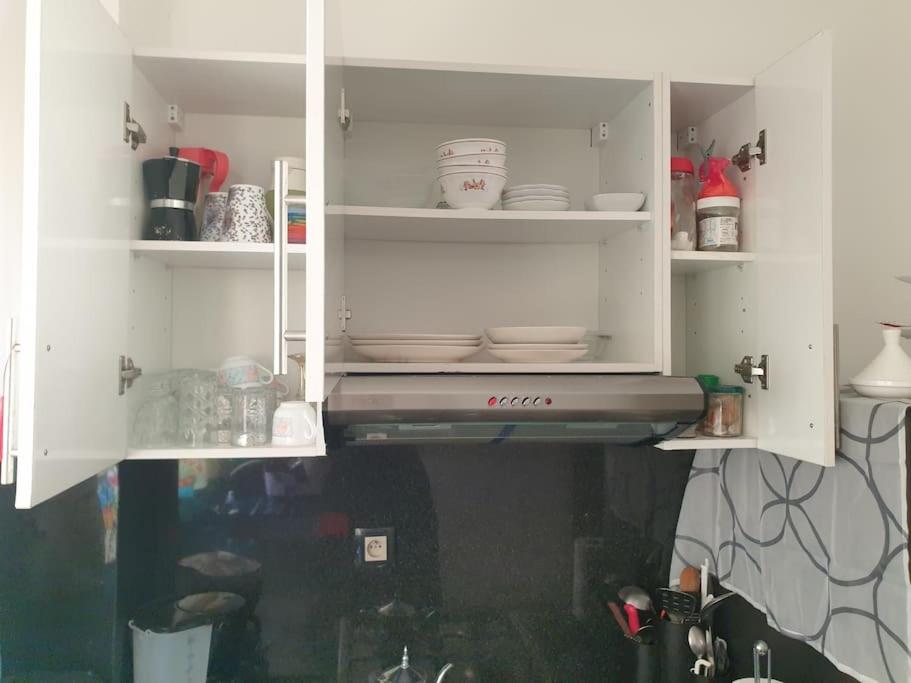 a kitchen with white cabinets with dishes in it at Appartement Cosy Disponible in Kenitra