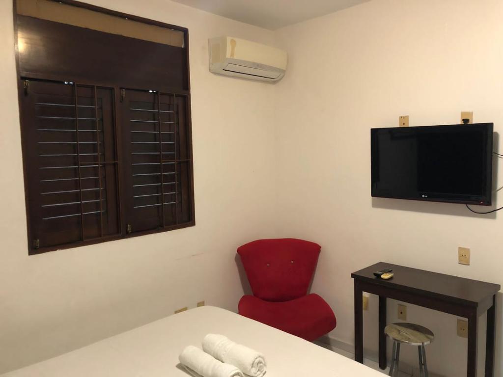 a room with a red chair and a flat screen tv at La Playa Hospedagem in João Pessoa