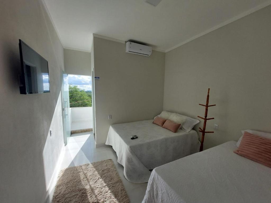Habitación blanca con 2 camas y TV en Pousada Luz do Sol en Piranhas