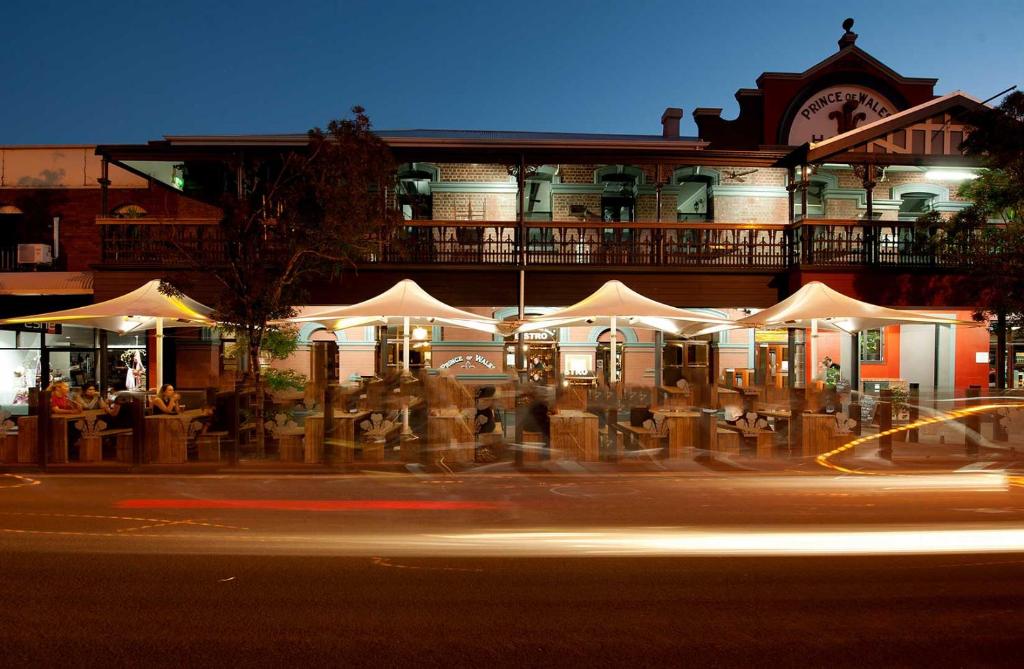 ein Gebäude mit Tischen und weißen Sonnenschirmen auf einer Straße in der Unterkunft Prince of Wales Hotel, Bunbury in Bunbury