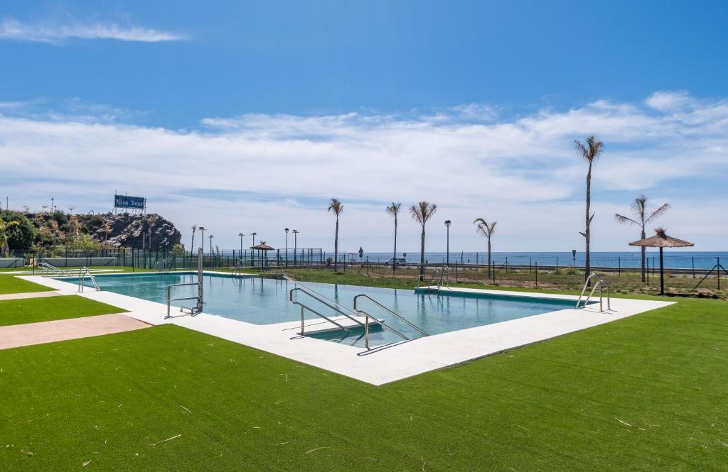una piscina con césped y palmeras en El amanecer, Apartamento 1 linea de playa en Vélez-Málaga