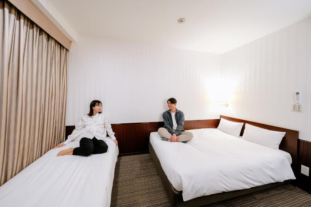 two people sitting on beds in a hotel room at Hotel Hillarys in Osaka