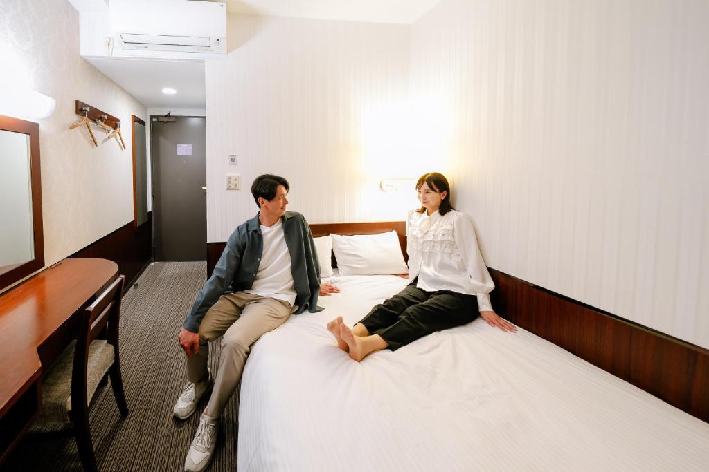 a man and a woman sitting on a bed at Hotel Hillarys in Osaka