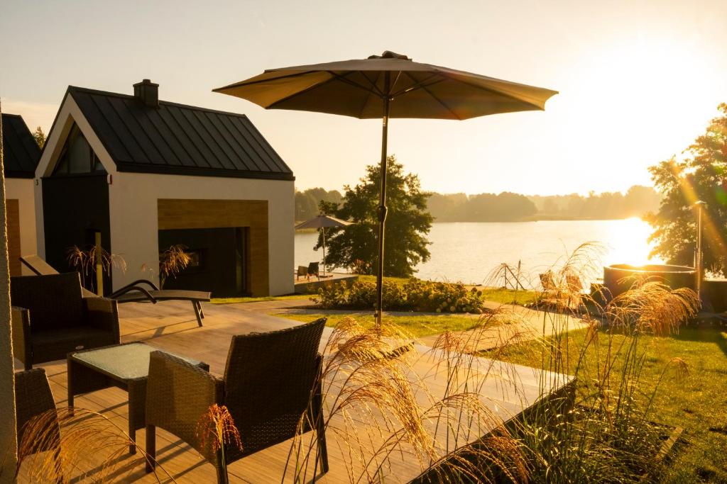 eine Terrasse mit einem Sonnenschirm und Stühlen neben einem See in der Unterkunft Warmiński Sad in Olsztyn