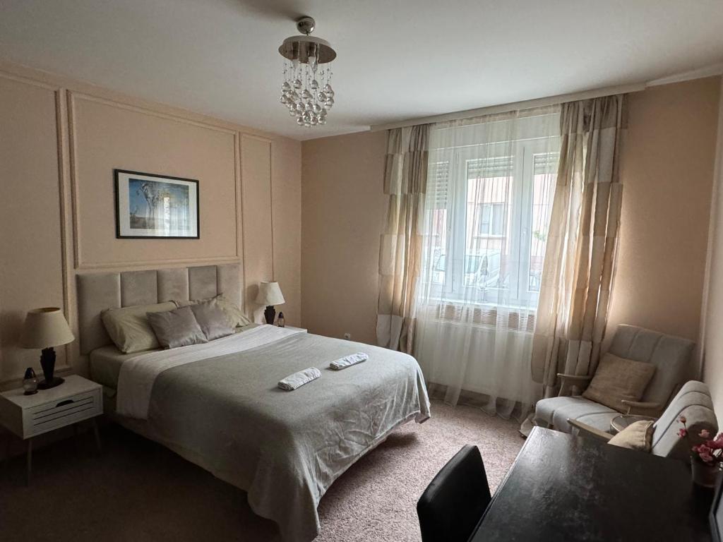 een slaapkamer met een bed, een stoel en een raam bij M2 Suite by Central Park in Kragujevac
