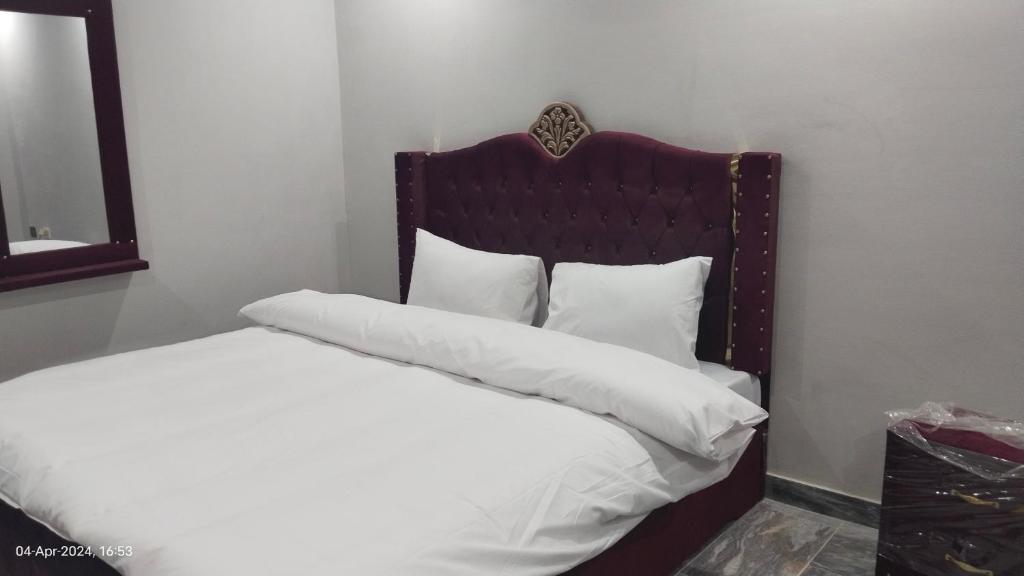 uma cama com lençóis brancos e almofadas num quarto em Hotel Crown Palace em Murree