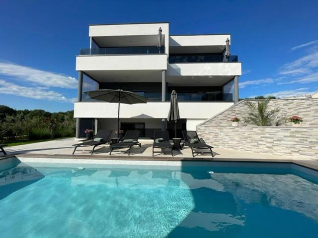 a house with a swimming pool with chairs and an umbrella at Villa Narona in Medulin