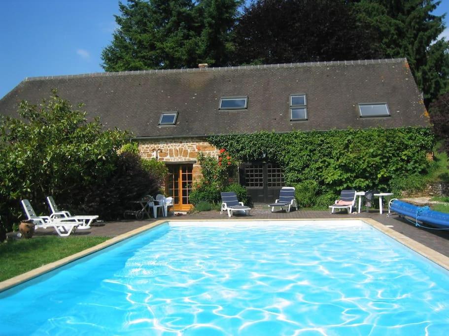 a large swimming pool in front of a house at Les Roses, avec piscine, tennis et lac privatif in Guerquesalles