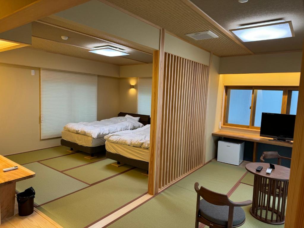 a bedroom with two beds and a desk and a television at Oshi Ryokan in Nagano