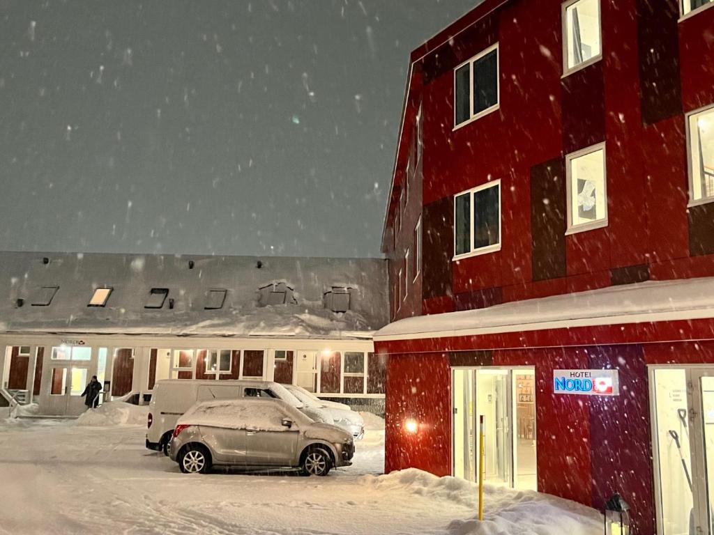 努克的住宿－Hotel Nordbo，雪中红色建筑前的汽车
