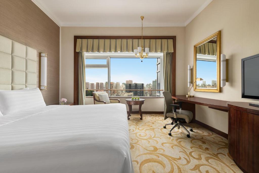 福州市にあるシャングリ ラ ホテル フージョウのベッド、デスク、窓が備わるホテルルームです。