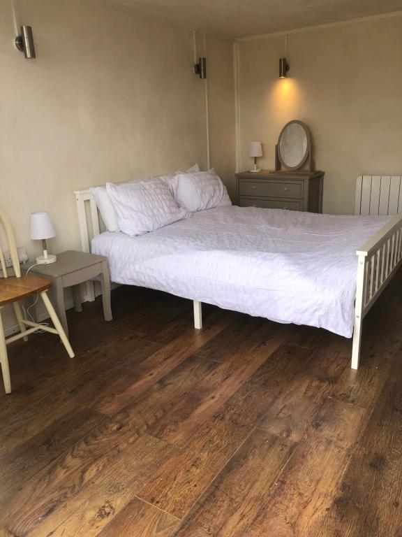 a bedroom with a white bed and a wooden floor at Bridport Garden Suite in Bridport