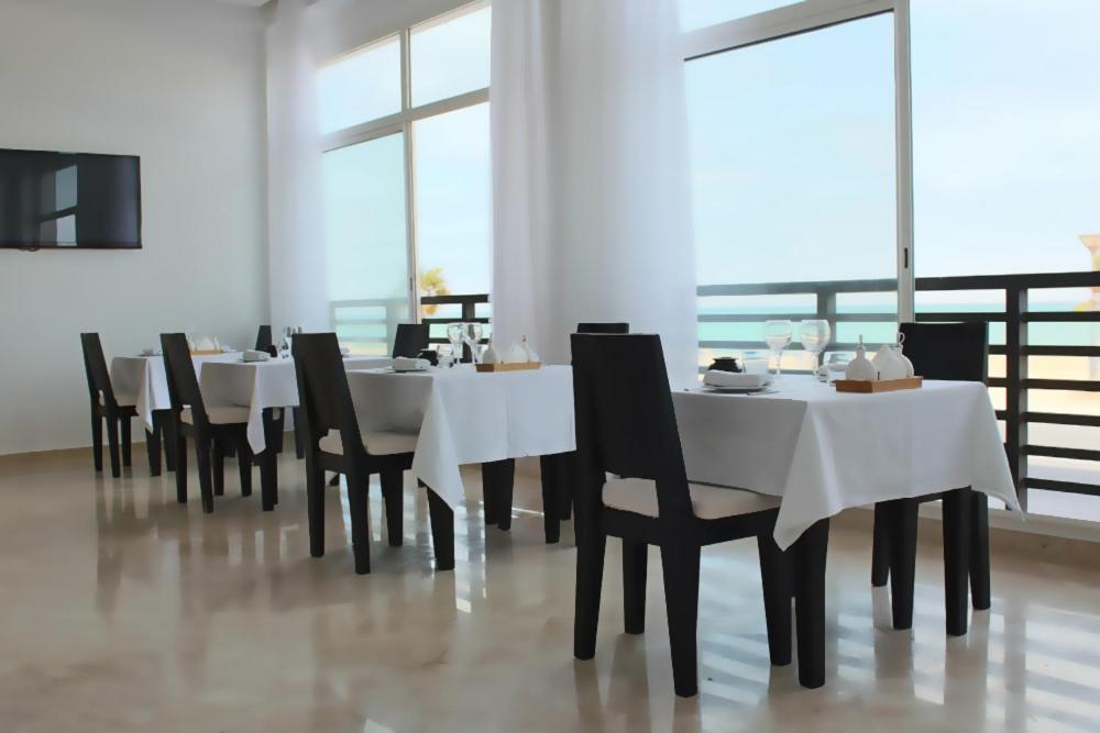 uma sala de jantar com mesas brancas e cadeiras pretas em Hotel Buenavista Dakhla em Dakhla