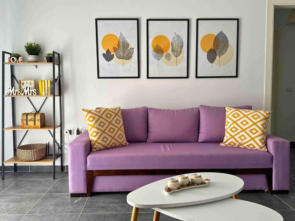 a purple couch in a living room with four pictures at Tropicana Apartments in Dhërmi