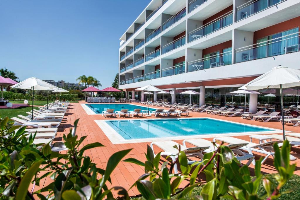 a hotel with a pool and chairs and umbrellas at Areias Village Beach Suite Hotel in Albufeira