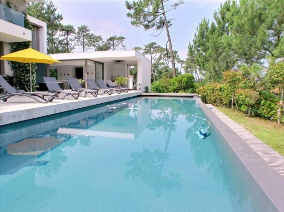 - une piscine avec des chaises et un parasol à côté d'une maison dans l'établissement Villa Contemporaine, GOLF AND SEA, Haut de gamme, Vue LAC, à Anglet
