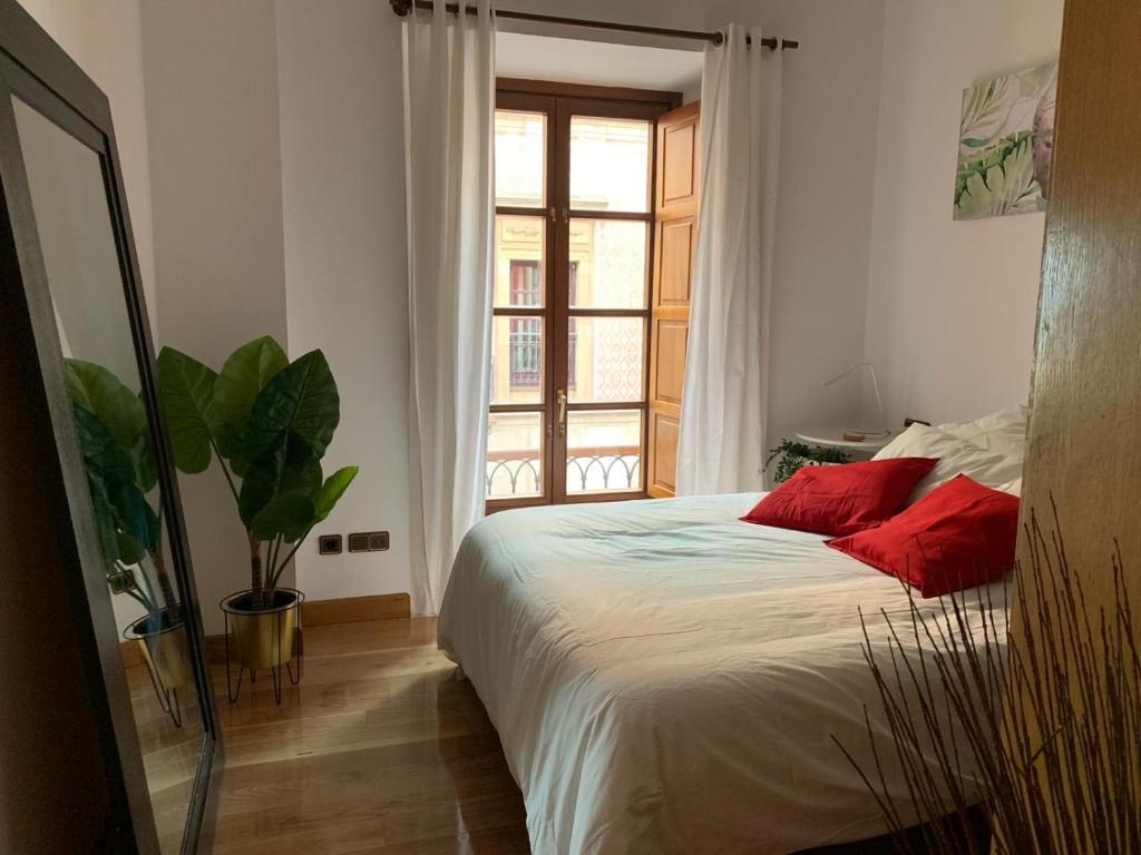a bedroom with a bed with red pillows and a window at MyHouseSpain - Acogedor apartamento plaza mayor Gijón 1 in Gijón