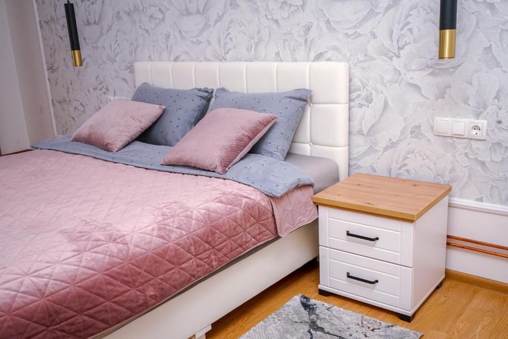 een bed met roze en blauwe kussens en een tafel bij Apartman Mona in Teslić