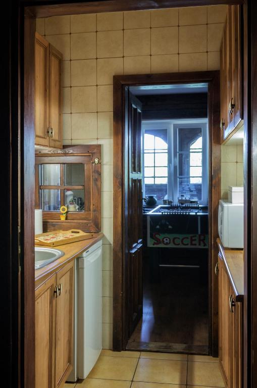 Narrow country kitchen with wooden cabinets, sink and dishwasher, doorway leading to dim game room.
