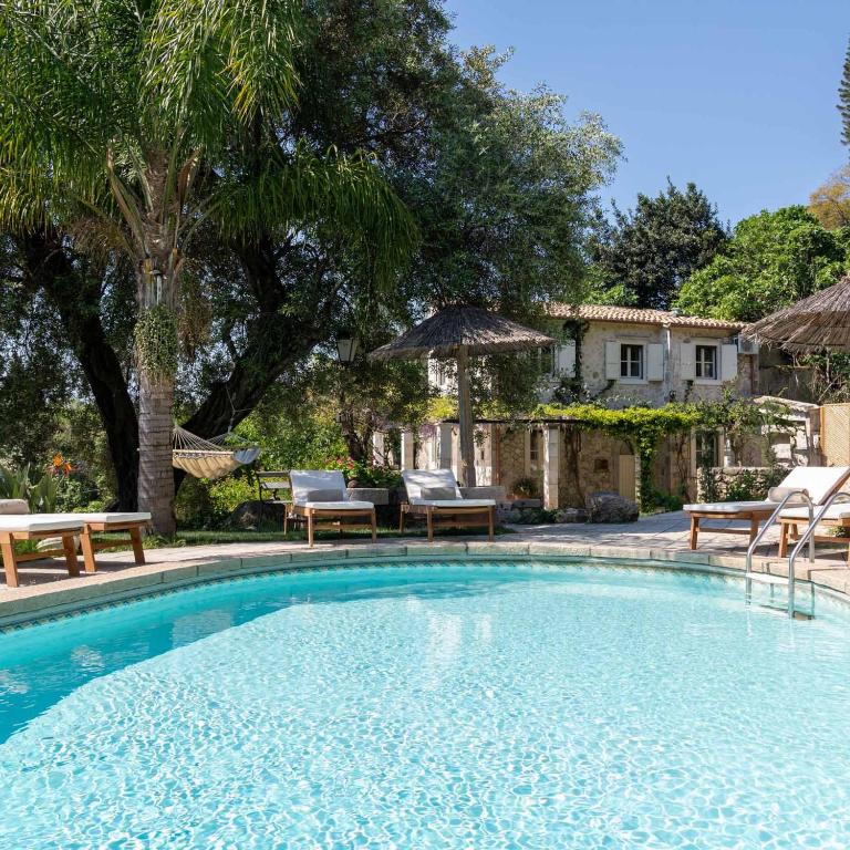 a swimming pool with chairs and a house at Corfu OliveStone Village with Swimming pool in Ágios Márkos